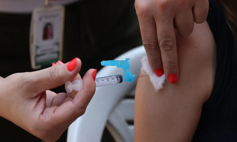 Uma pessoa com uma seringa na mão faz aplicação de vacina numa outra pessoa. Foto: José Cruz/Agência Brasil